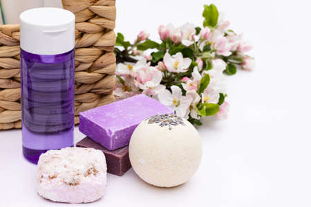 Lilac cosmetic bottle, bath bomb, handmade soap, bath salt near wicker basket with pear flowers on a...
