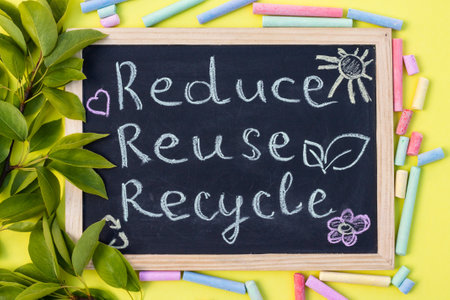 Chalk board Reduse Reuse Recycle sign on a yellow background with green leaves and chalk pieces. Top viewの写真素材