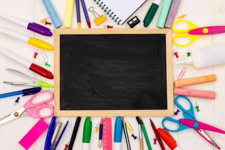Back to school black chalk board on a white wooden background, color supplies. Top view. Copy space. Education concept.の写真素材