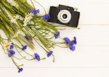Retro vintage old camera with cornflowers and daisies on a white wooden background. Top view. Copy space.の写真素材