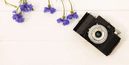 Retro vintage old camera with cornflowers on a white wooden background. Top view. Copy space. Bannerの写真素材