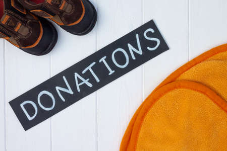 Children's plaid and boots with a chalk Donations sign on a white wooden table. Flat lay. Charity and donation concept.の写真素材
