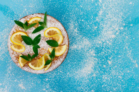 Lemon pie with lemon slices, mint and powdered sugar on a blue background. Top view, copy space.