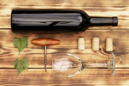 Wine glass, corkscrew, corks, wine bottles, grapevine on rustic burnt wooden background. Top view,...