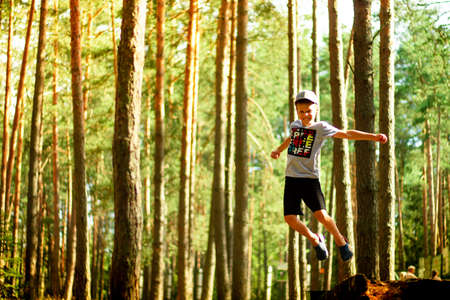 Laughing boy 7-10 in shorts and a T-shirt jumps in a pine forest in rays of sunlight.の写真素材