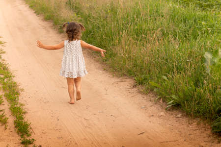 Little cute girl 1-3 in a light dress running on a path in the field on a background of grass in summerの写真素材