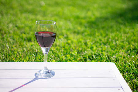 Glass with red wine on a white wooden table on a background of grass, copy spaceの写真素材