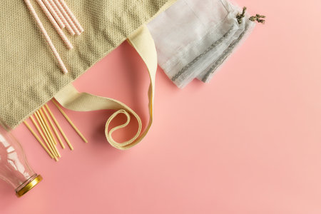 Fabric cotton shopping bags, glass bottles and jars, paper straws and wooden sticks on a pink...