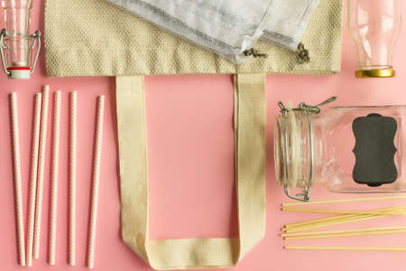 Fabric cotton shopping bags, glass bottles and jars, paper straws and wooden sticks on a pink background. Zero waste and ecological concept. Top view. Copy space.の写真素材