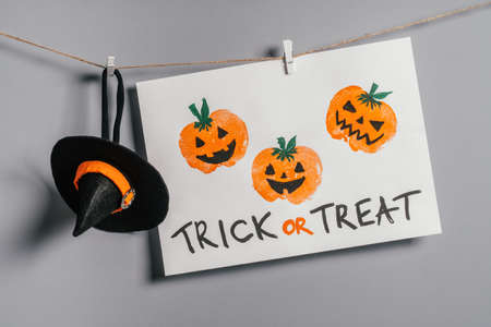 Halloween childrens pumpkin apple prints drawing hanging on rope on gray wall with Treat or Treat inscription and witch hatの写真素材
