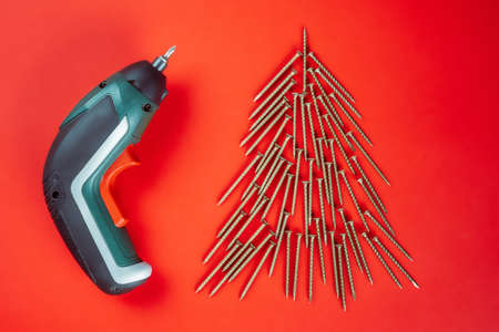 Long golden self-tapping screws, laid out in shape of Christmas tree and screwdriver on red backgroundの写真素材