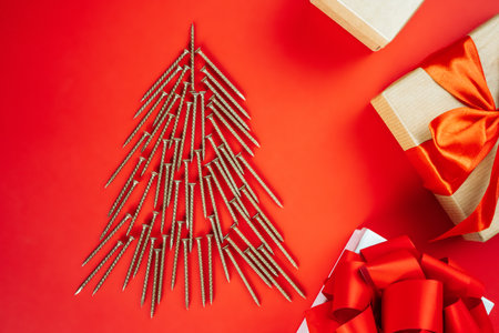 Long golden self-tapping screws, laid out in shape of Christmas tree and gift boxes on red backgroundの写真素材