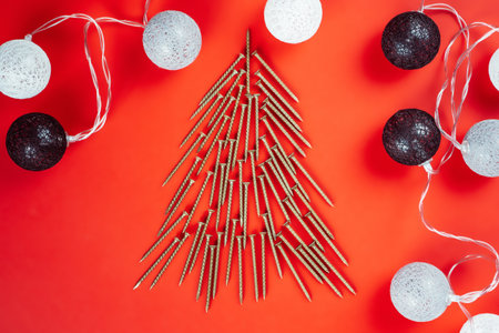 Long golden self-tapping screws, laid out in shape of Christmas tree and ball garland on red backgroundの写真素材