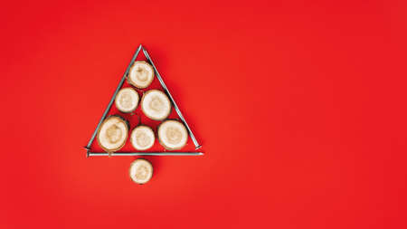 Long nails and wood cuts or branch slabs, laid out in shape of Christmas tree on red background. Banner. Flat lay. Copy spaceの写真素材