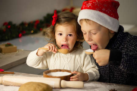 Cute little girl 2-4 with a red bow and boy 7-10 in a Christmas cap, making Christmas gingerbread...