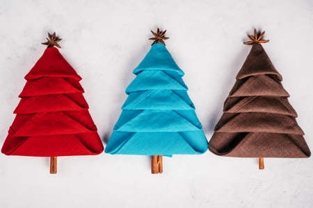 Three linen napkins folded in shape of Christmas trees on white concrete surface. New Year table setting. Top view.の写真素材