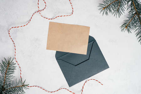 Green open envelope on white concrete background with blank kraft paper greeting card with branches of Christmas tree. New year envelope with untied cord. Copy space. Top viewの写真素材
