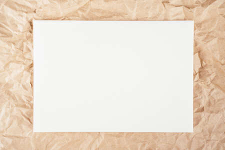 Background image of rough crumpled recycled textured kraft paper with sheet of white cardboard in...