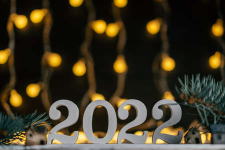 Happy New Year 2022. White wooden numbers 2022 stand on white surface with Christmas tree branches against background of garland light bulbs. Merry Christmas. Copy spaceの写真素材