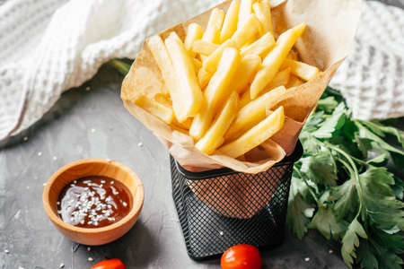 Large serving of French fries stand in craft paper with barbecue sauce, sesame seeds, cherry...