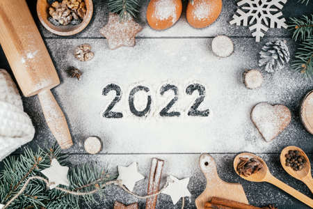 Numbers 2022 written on flour sprinkled on black table with branches of Christmas tree, baking...