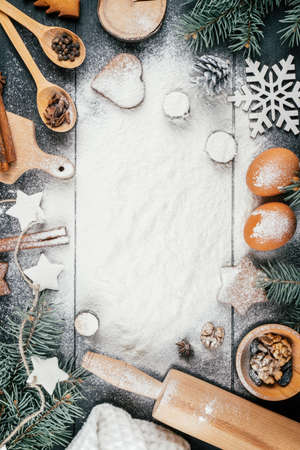 Branches of Christmas tree, gingerbread cookies, baking accessories and ingredients lying on black wooden table with sprinkled flour. Copy space. Merry Christmas and Happy New Year. Top view. Verticalの写真素材