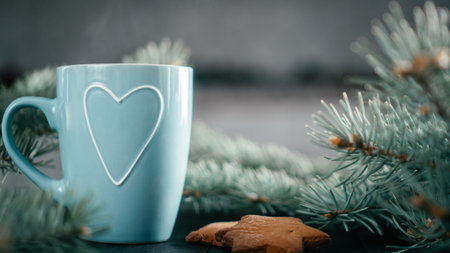 Partially blurred blue cup with heart with Christmas tree branches and gingerbread cookies. Copy...