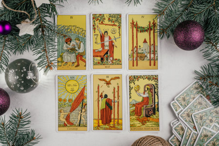 Tarot cards spread face up on white concrete surface with Christmas tree branches and decorations....