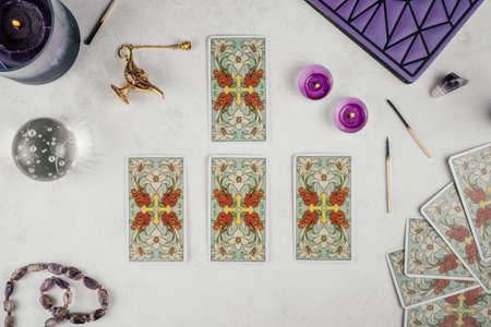 Tarot cards spread face down on white concrete surface with crystal ball, candles and attributes....