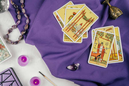 Tarot cards spread face up on purple cloth on white concrete surface with candles and attributes. Top view. Minsk, Belarus, 11/19/2021のeditorial素材