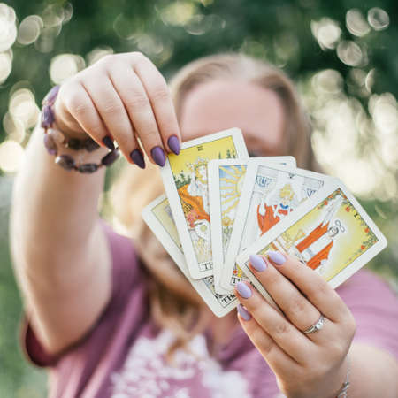 Female hands with bracelet and purple nails hold fan of tarot cards facing and touch one of them. Minsk, Belarus, 28.07.2021のeditorial素材