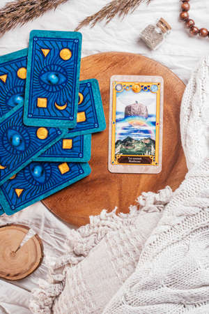 Deck of Tarot spread with one open card on wooden tray on white cloth sheet with pillows, bedspread and spikelets. Vertical. Top view. Minsk, Belarus - 09/27/2021のeditorial素材