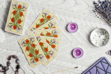 Tarot cards spread face down on white knitted surface with crystal ball, lavender, candles and...