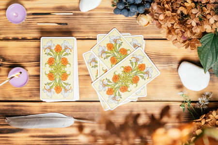 Tarot cards spread face down on wooden surface with candles, stones, autumn plants and accessories....