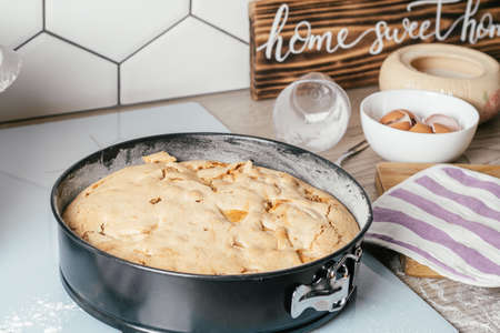 Baking dish with baked apple pie stands on kitchen counter next to ingredients, cooking utencils and wooden sign Home sweet homeの写真素材