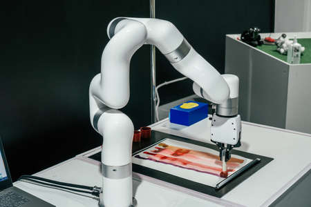 Partially blurred robot with automatic gripping claws and many joints, able to grip and control various objects. Robot holds paintbrush and draws stripes on sheet of paperの写真素材