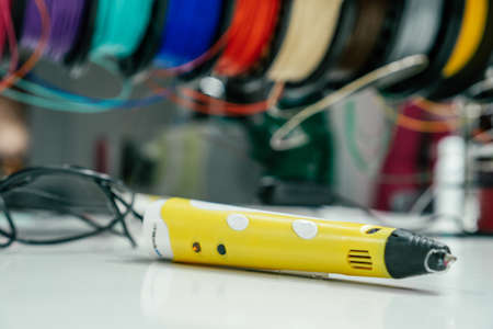 Blurred yellow 3D pen lying on white table with skeins of colored plastic behind itの写真素材