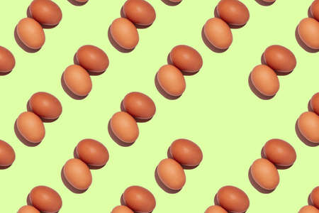 Pattern of beige egg pairs with hard shadows isolated on light green background. Top view. Copy spaceの写真素材