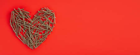 Small metal nails laid out randomly in shape of heart on red background. Broken heart relation concept. Banner. Flat lay. Copy space. Mock upの写真素材