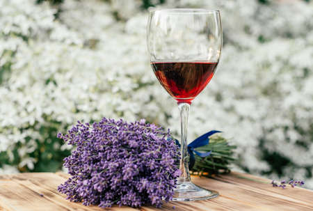 half-empty glass of red wine and lavender bouquet tied with blue ribbon on wooden brown table in...