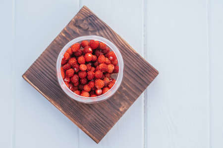 Fresh ripe juicy peeled strawberries in transparent glass round bowl on brown wooden square board on light blue background. Healthy food. Copy space. Top view. Mock up.の写真素材