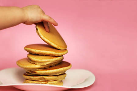 A child takes a pancake from a stack, pink background. American delicious pancakes. Close up, copy...