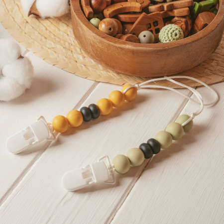 White plastic clothespin with white, black and orange wooden beads on white laces for baby pacifiers...