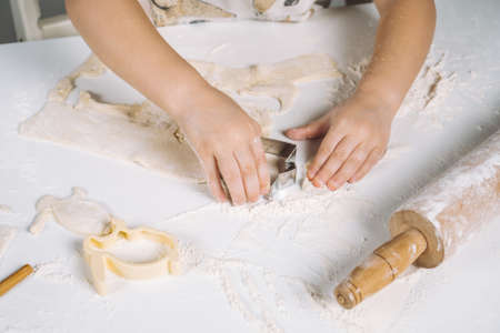 Cropped photo of little child kid hands, cutting different shape dough cookies by metallic backing...