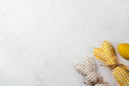 Easter postcard for celebration holiday, two handmade square brown, white and yellow colored bunnies with strings-scarfs on white gray paper background, yellow chicken egg. Copy space, place for text.の写真素材