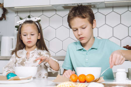 Portrait of concentrated two little children, boy, girl, multi coloring Easter hens eggs. Soaking...
