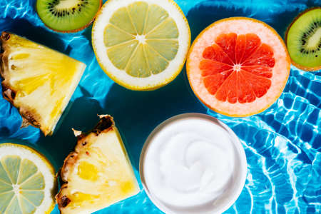 Facial jar cream milky beauty product in fruit citrus lemon, kiwi, orange, pineapple in water splashing fresh transparent, flecks. Flat lay, top view. Summer beach tropical. Skin care in summerの写真素材