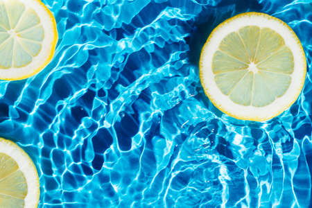 Transparent fresh exhilarant wave water with flecks background, lemon citrus slices. Summer freshness, healthy eating beach travel drinks concept. Vitaminic moisturizing care. Flat lay, copy spaceの写真素材