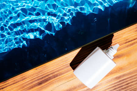 Wood desk with white bottle of nose drops, allergy aerosol for sinusitis cure. Control breath. Blue transparent reflect water surface ocean. Hot warm dry air summer beach. Flat lay. Place for text.の写真素材