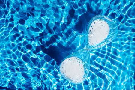 Blue abstract glass hourglass with white sand in water reflect surface pool. Renovation of time....